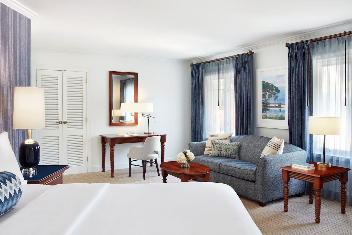 A hotel room with a bed, a desk, a chair, a sofa, and two lamps.