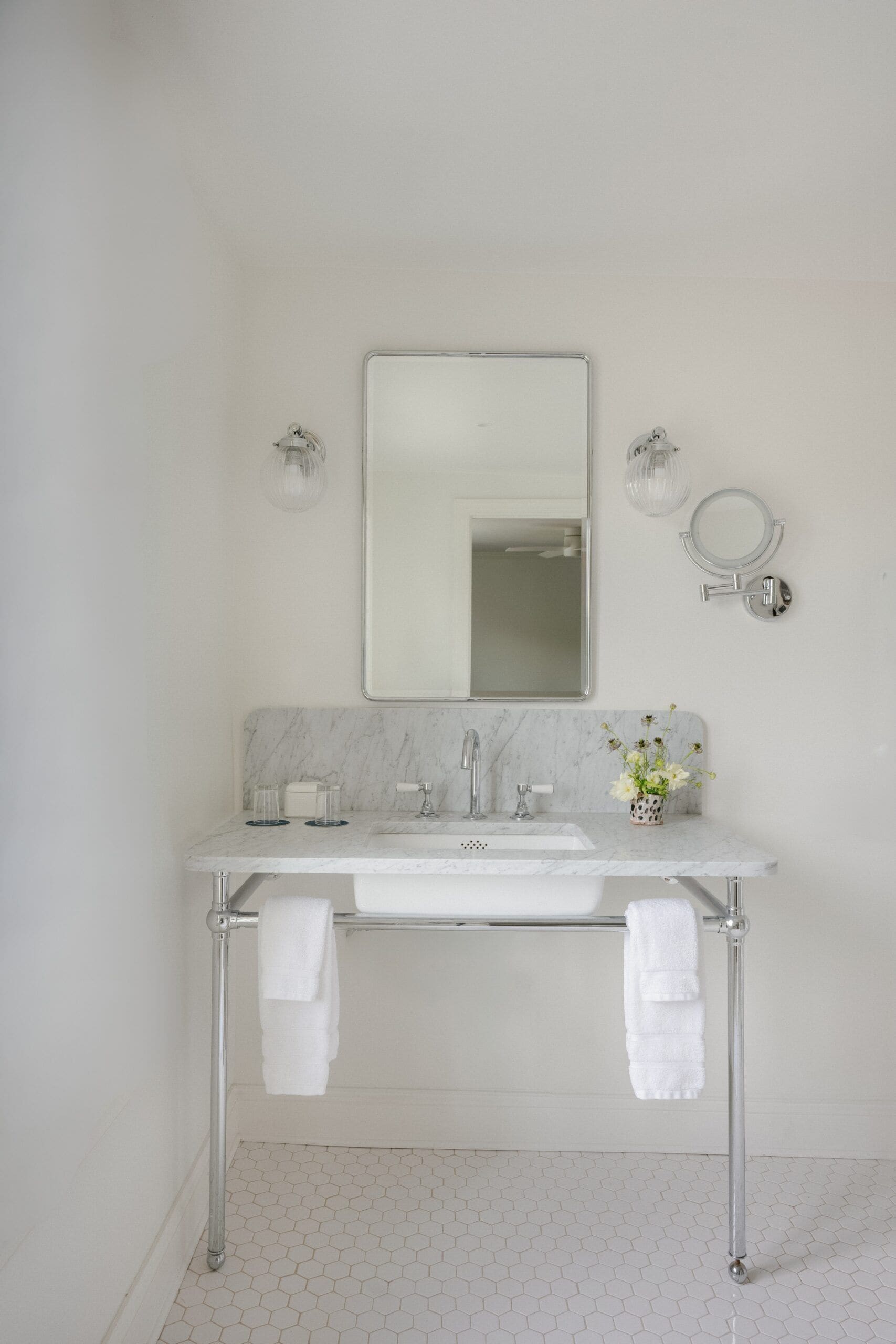 A bathroom with a marble countertop, a sink, a mirror, and two towel racks.