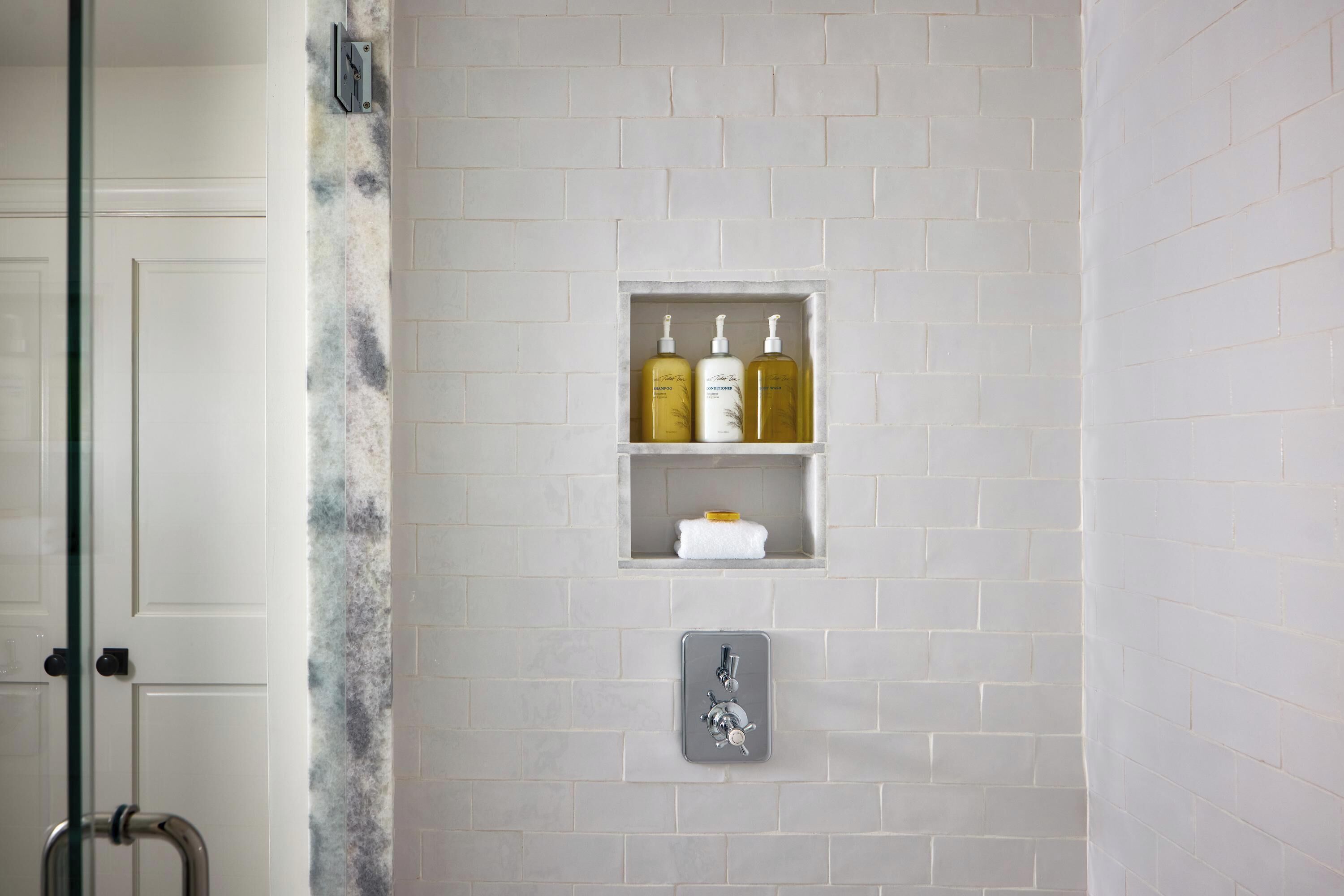 A bathroom with a shower, a towel rack, and a shelf with toiletries.
