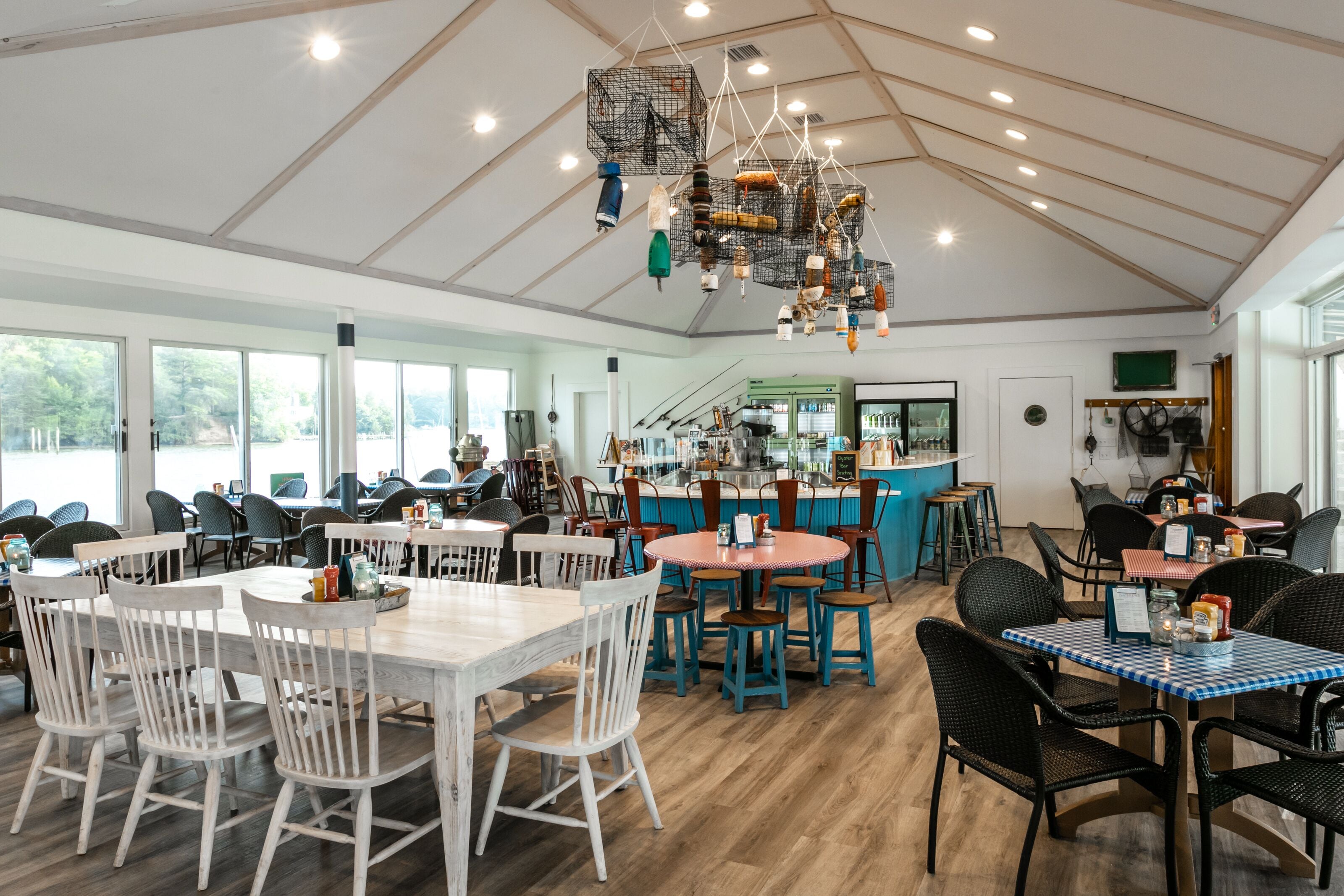 A spacious restaurant with high ceilings, wooden beams, and a variety of seating options including white and black chairs and tables.