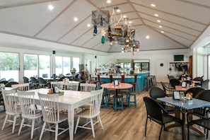 Ein großzügiges Restaurant mit hohen Decken, Holzbalken und vielfältigen Sitzmöglichkeiten, darunter weiße und schwarze Stühle sowie Tische.