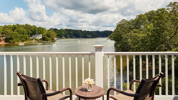 A balcony with two chairs and a table, overlooking a river with boats and houses in the background. - The Tides Inn (Irvington)
