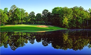 Ein Golfplatz mit einem Teich, der Bäume und Himmel spiegelt.