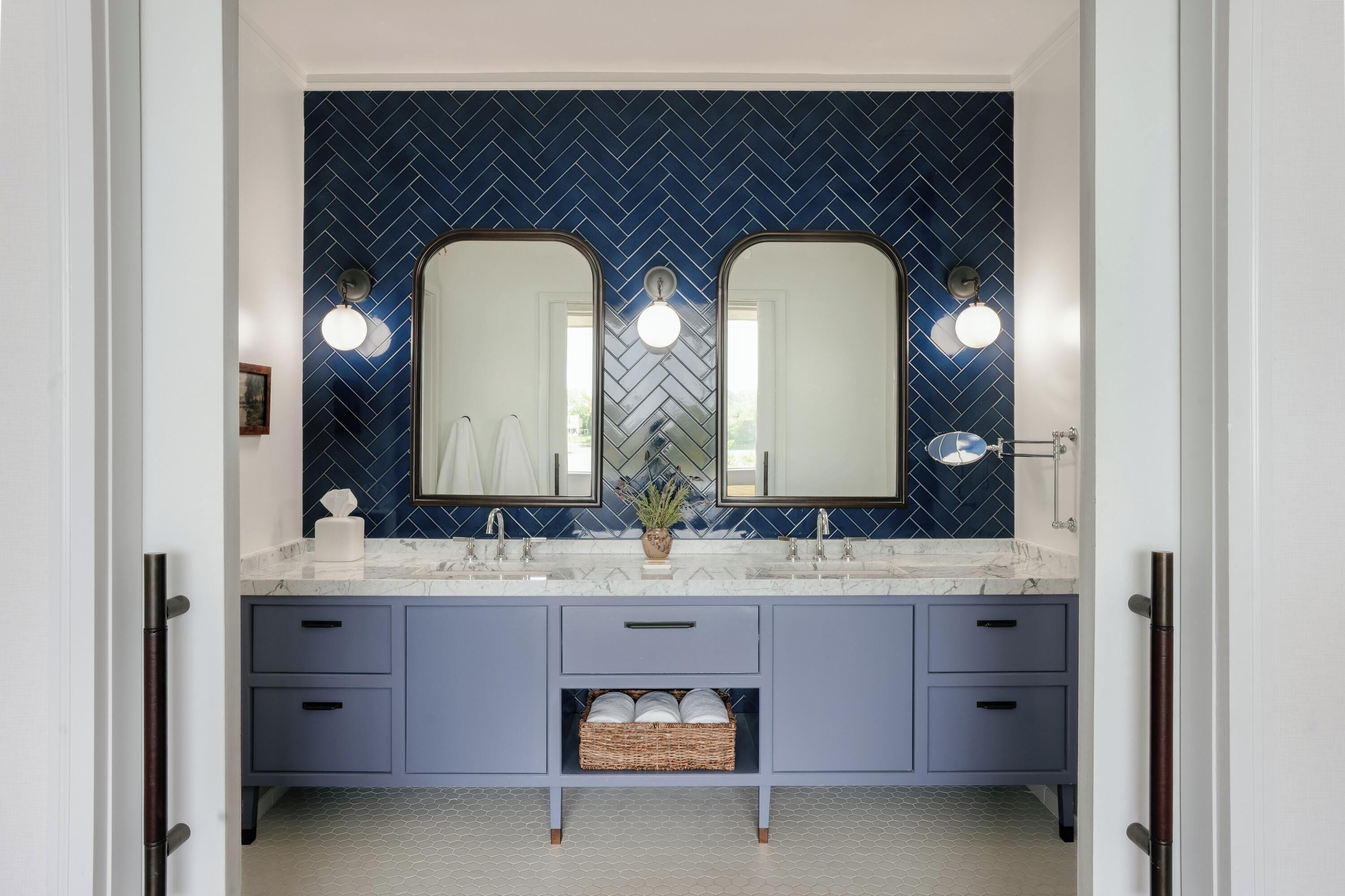 A bathroom with a double vanity, two mirrors, and a herringbone patterned backsplash.
