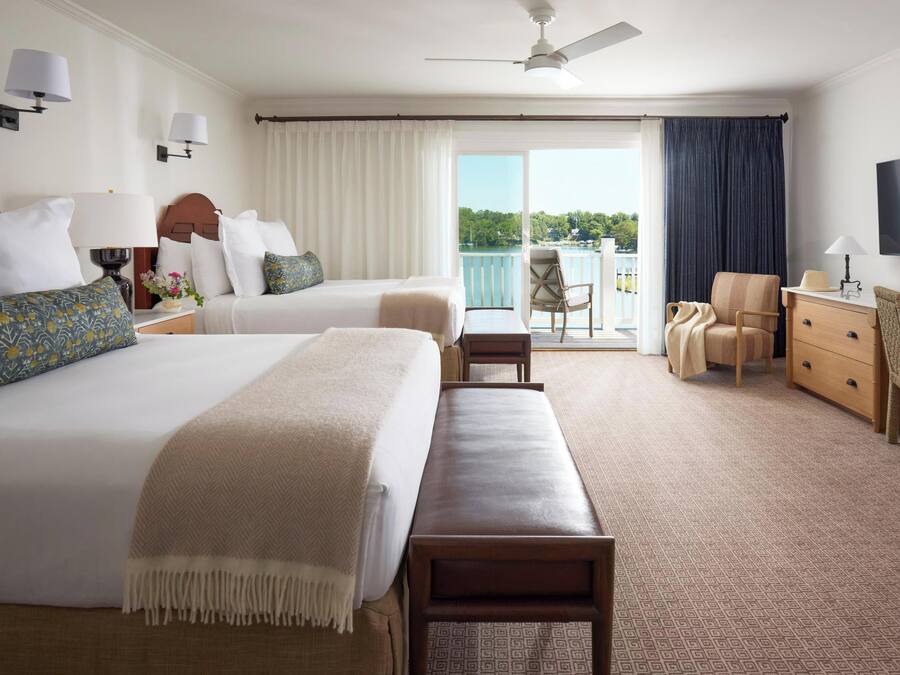 A hotel room with two beds, a balcony, a TV, and a desk.