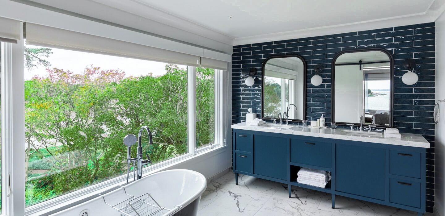 Un baño moderno con un ventanal grande, una bañera independiente y muebles de color azul oscuro.