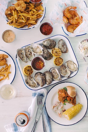 A variety of seafood dishes including oysters, shrimp, and fried items, served on multiple plates and trays.