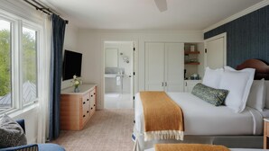 A hotel room with a bed, a desk with a flat-screen TV, a bathroom visible through an open door, and a view of the outdoors. - The Tides Inn (Irvington)