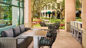 An outdoor patio with wicker furniture, a wooden table, and a view of a building with a green awning.