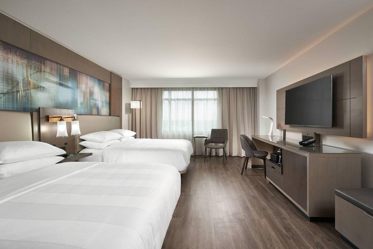 Ein Hotelzimmer mit zwei Betten, einem Schreibtisch, einem Sessel, einem Fernseher und einem Bild an der Wand.