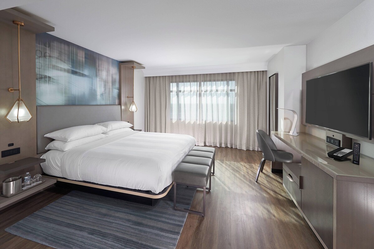 Habitación de hotel moderna con una cama grande, un escritorio, un televisor de pantalla plana, un banco y un cuadro en la pared.