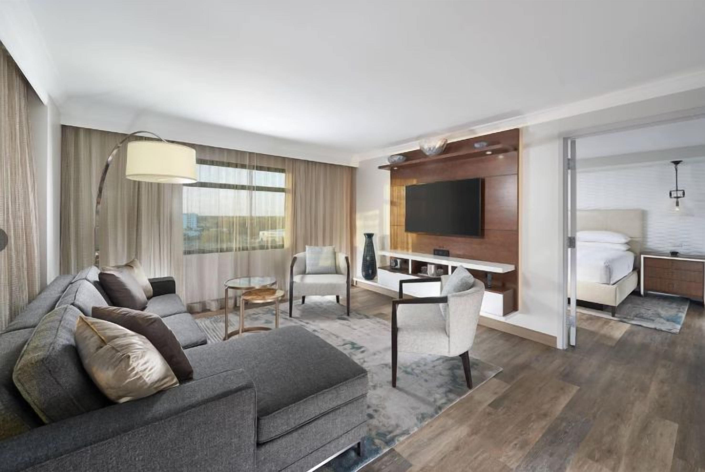 Una habitación de hotel moderna con un conjunto de sofás, una mesa de comedor, un televisor montado en la pared y una zona de dormitorio separada.
