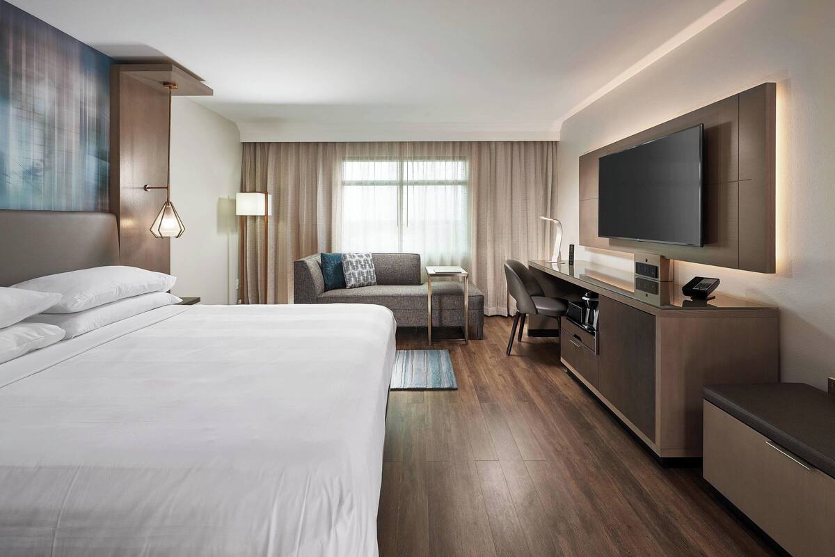 Ein Hotelzimmer mit einem großen Bett, einem Schreibtisch, einem Flachbildfernseher und Blick ins Freie durch ein Fenster.