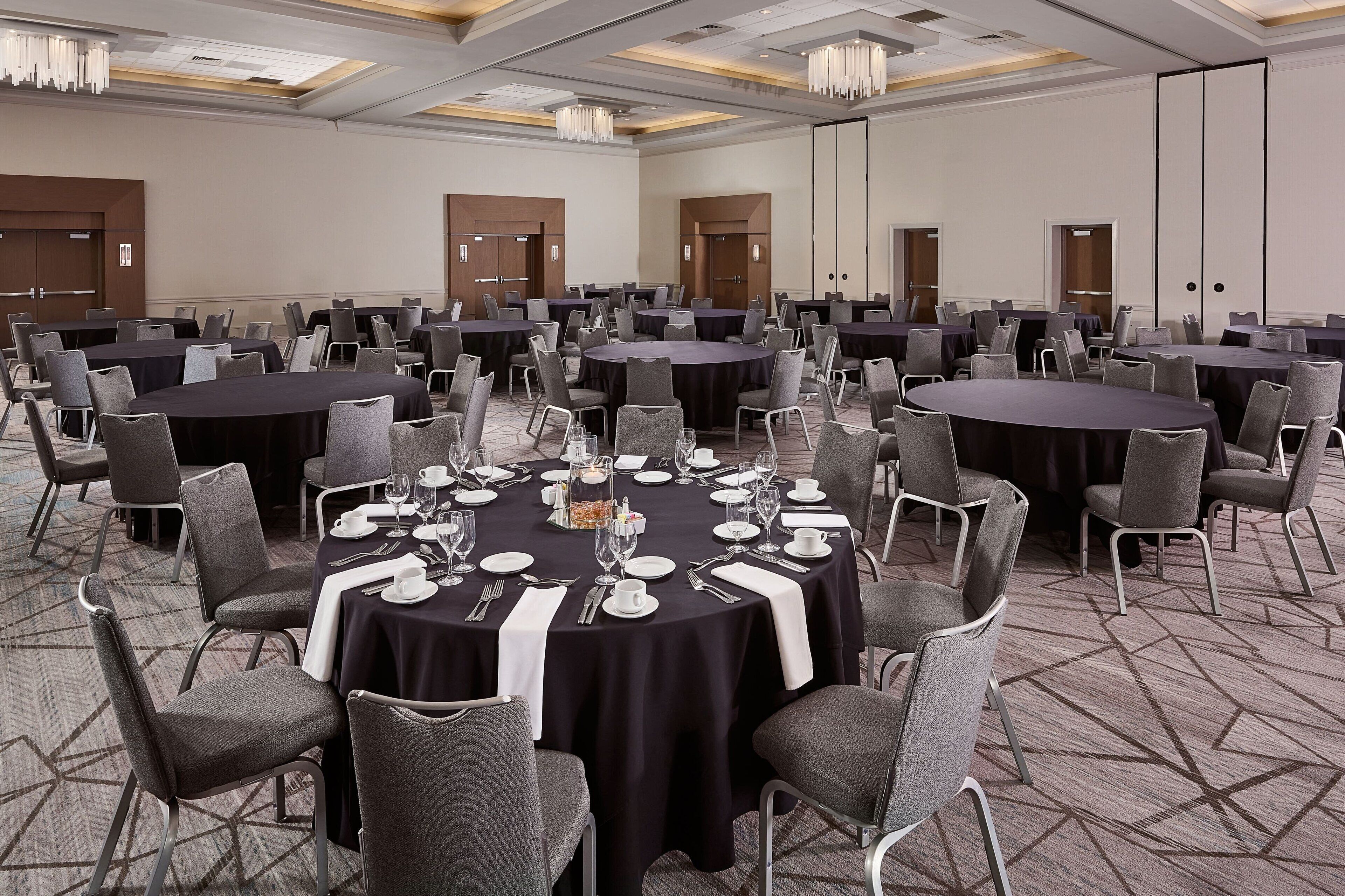 Un salón de conferencias con varias mesas redondas, cada una con sillas, platos, cubiertos y copas de vino.