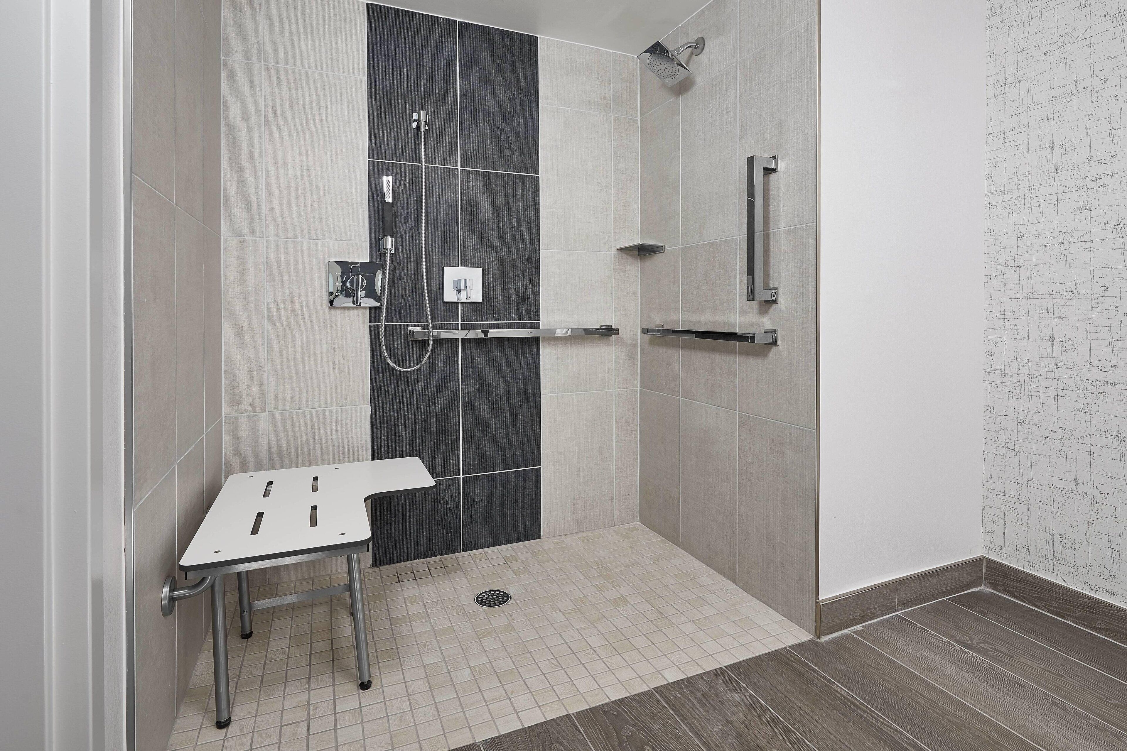 A shower area with a bench, a handheld showerhead, and a wall-mounted towel rack.