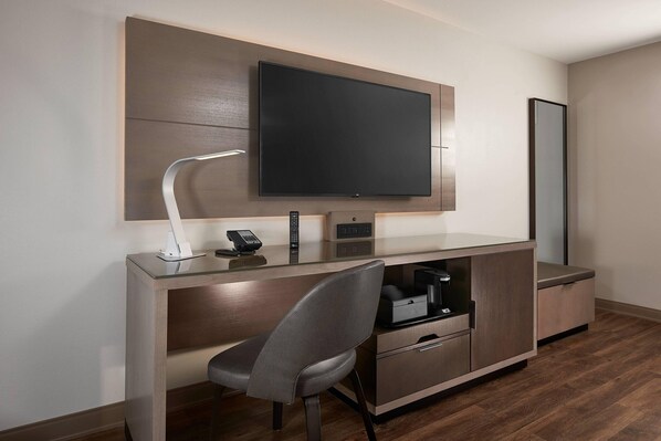 Una habitación de hotel moderna con un televisor de pantalla plana montado en la pared, un escritorio con una silla, una cafetera y un teléfono.