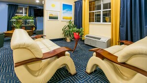 A cozy room with two beige armchairs, a wooden coffee table, a potted plant, and a large window with curtains. - Days Inn & Suites by Wyndham Pryor (Pryor)