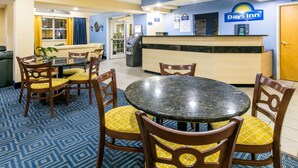 A Days Inn reception area with a reception desk, chairs, a small dining table, and a patterned carpet. - Days Inn & Suites by Wyndham Pryor (Pryor)