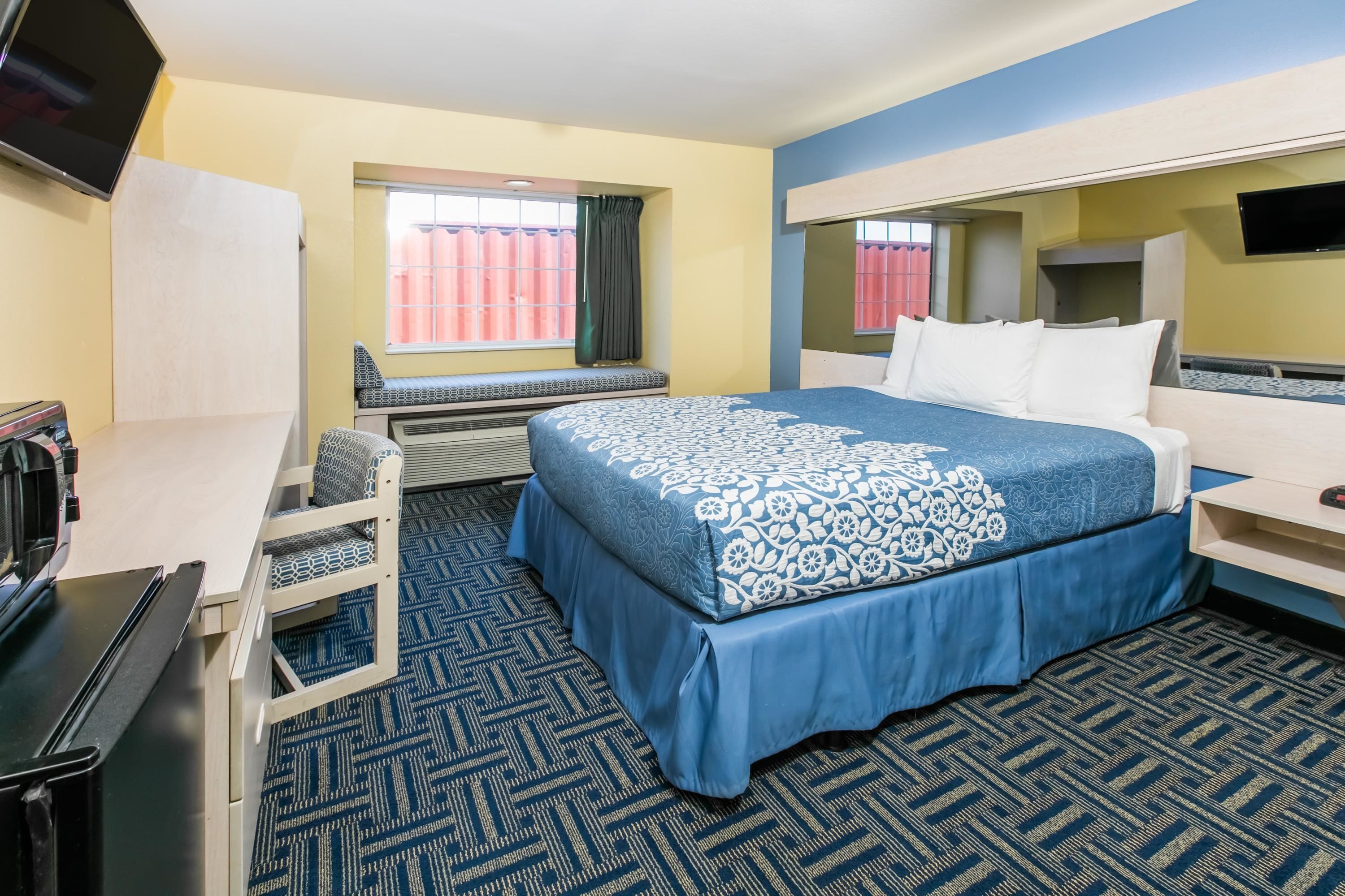 Habitación de hotel con cama, escritorio, silla, televisor y ventana con cortinas.