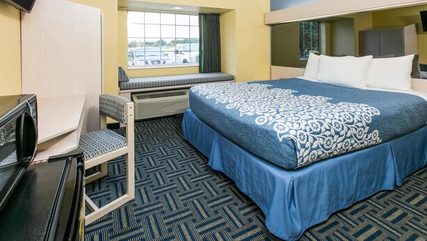 A hotel room with a large bed, a desk with a chair, a window with a view of parked cars, and a built-in TV. - Days Inn & Suites by Wyndham Pryor (Pryor)
