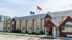 A multi-story hotel with a red and beige exterior, a parking lot, and two flags on flagpoles. - Days Inn & Suites by Wyndham Pryor (Pryor)