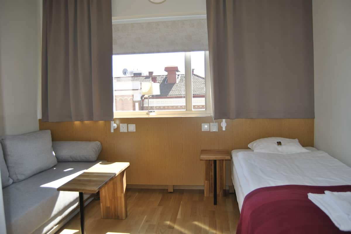 A compact room with a bed, a sofa, a small table, and a window with curtains.