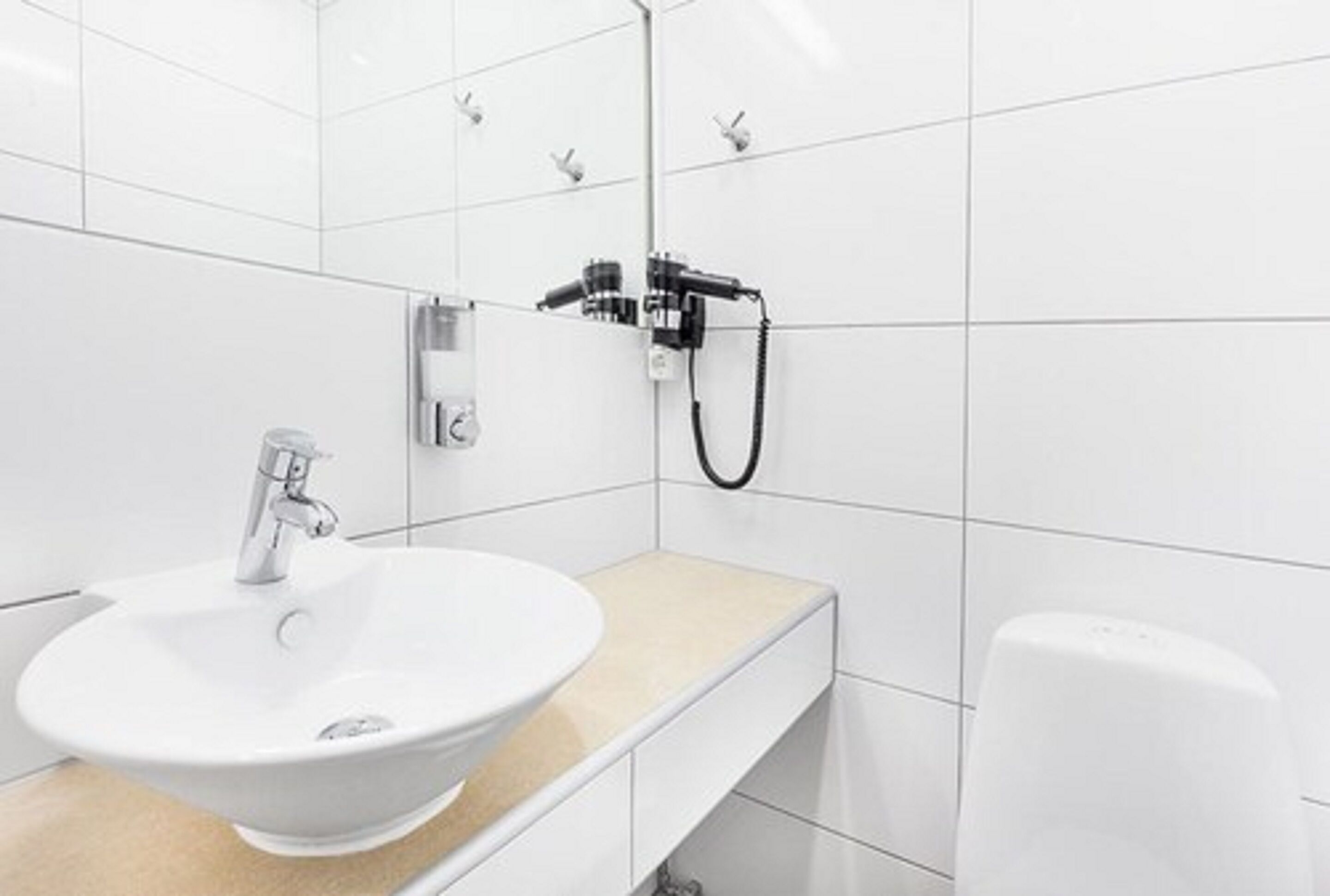 Et moderne badeværelse med en hvid vask, brusehoved og sæbedispenser.