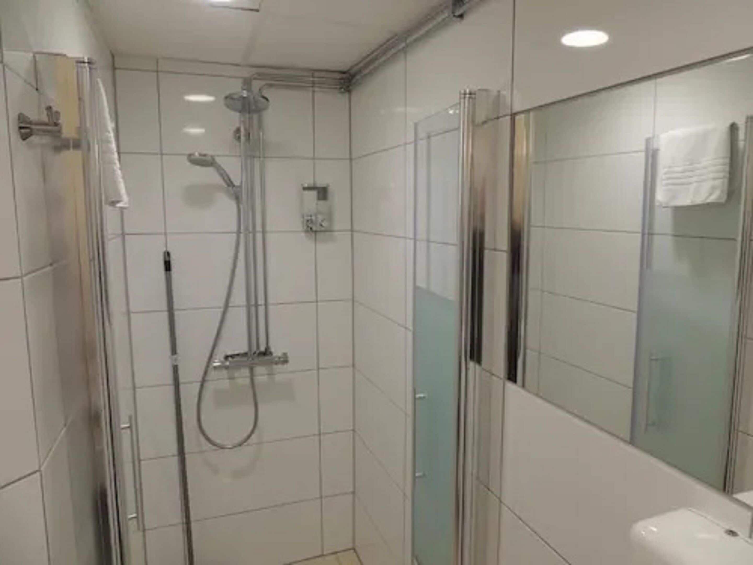 A modern bathroom with a glass shower enclosure, a handheld showerhead, and a wall-mounted faucet.