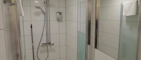 A modern bathroom with a glass shower enclosure, a handheld showerhead, and a wall-mounted faucet.