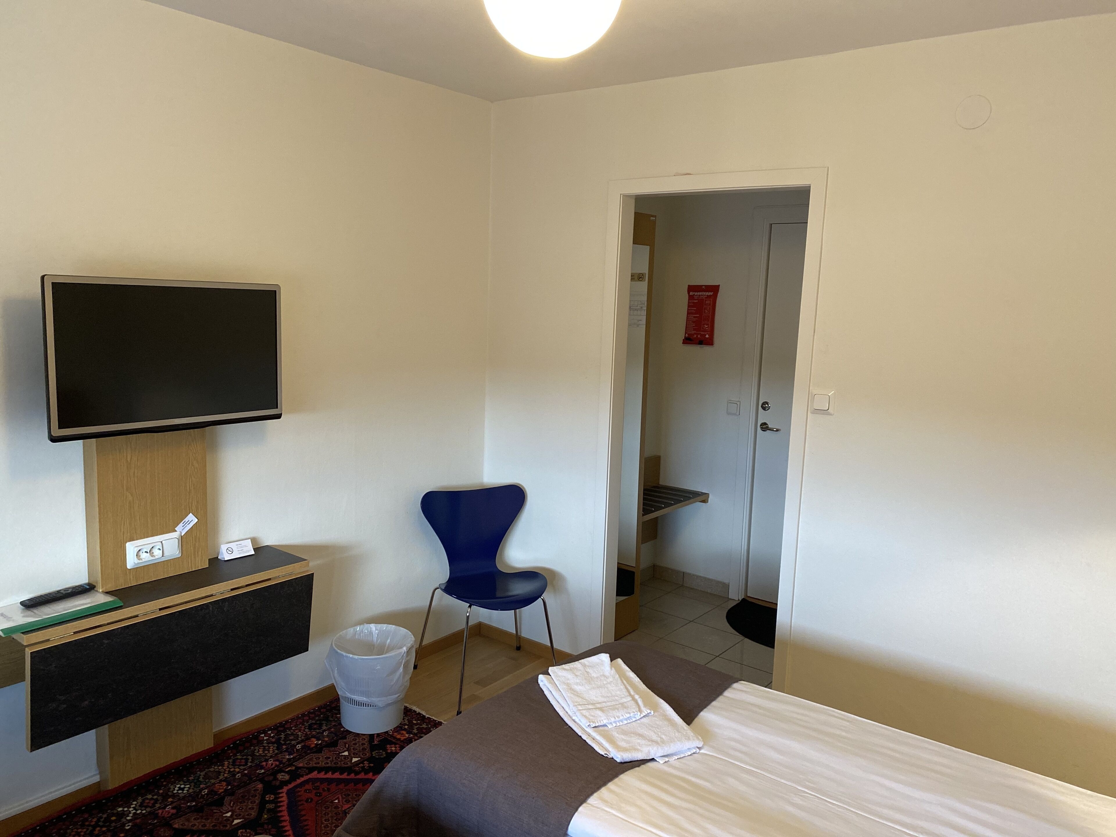 Ett hotellrum med en säng, ett skrivbord med en tv, en stol och en papperskorg.