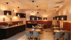 A restaurant with wooden paneling, black pendant lights, and a buffet area with a coffee machine. - Ronneby Cityhotell (Ronneby)