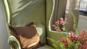 A green armchair with a brown cushion, a small round table with a white mug, a green apple, a magazine, and a vase with pink flowers. - Ronneby Cityhotell (Ronneby)