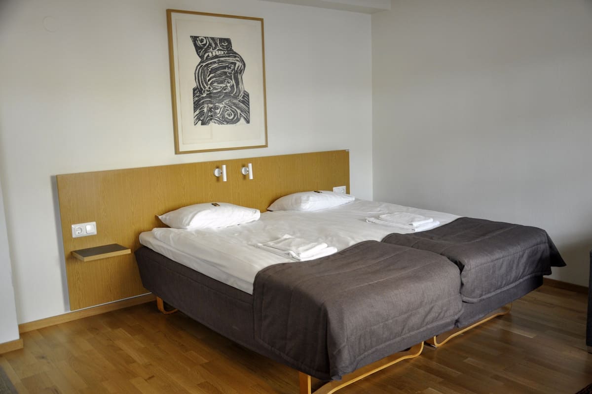 A double bed with a wooden headboard, white linens, and a gray blanket.