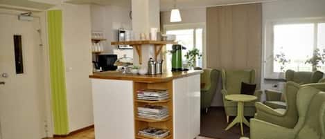 A modern living room with a central coffee station, green armchairs, and a small side table.