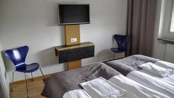 Une chambre d’hôtel avec deux lits, un téléviseur fixé au mur et deux chaises bleues.