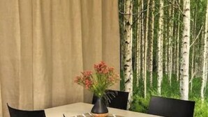 A dining area with a table and chairs, a vase with flowers, and a backdrop of birch trees. - Ronneby Cityhotell (Ronneby)