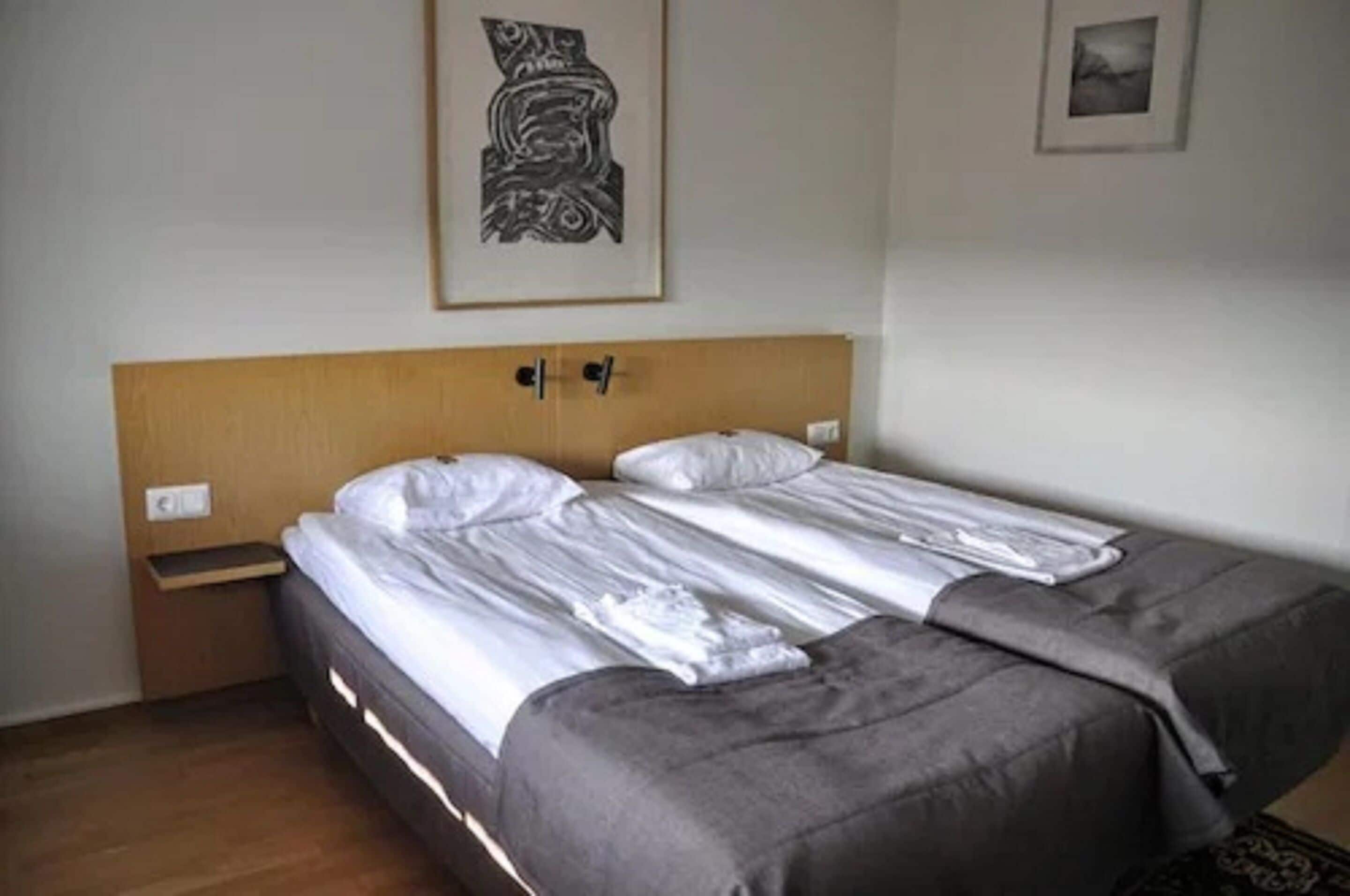 A double bed with a wooden headboard, two bedside tables, and a gray blanket.