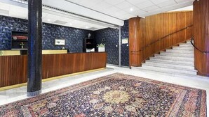 A reception area with a wooden reception desk, a large patterned rug, and a staircase. - Ronneby Cityhotell (Ronneby)