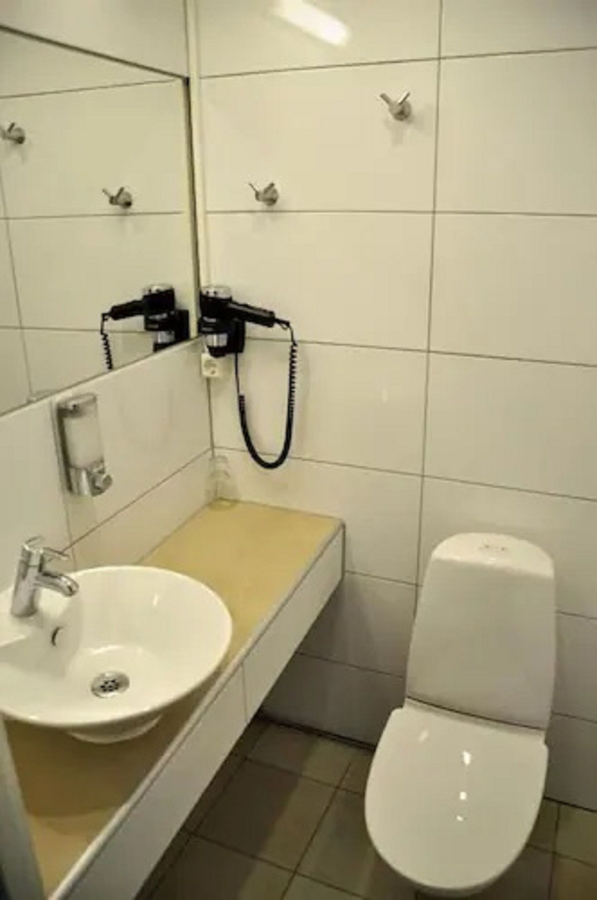 A small bathroom with a white sink, a mirror, a toilet, and a hairdryer on the wall.