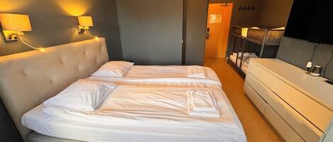 Habitación de hotel con cama doble, lámparas de noche, televisión, cómoda y puerta que da a otra habitación.