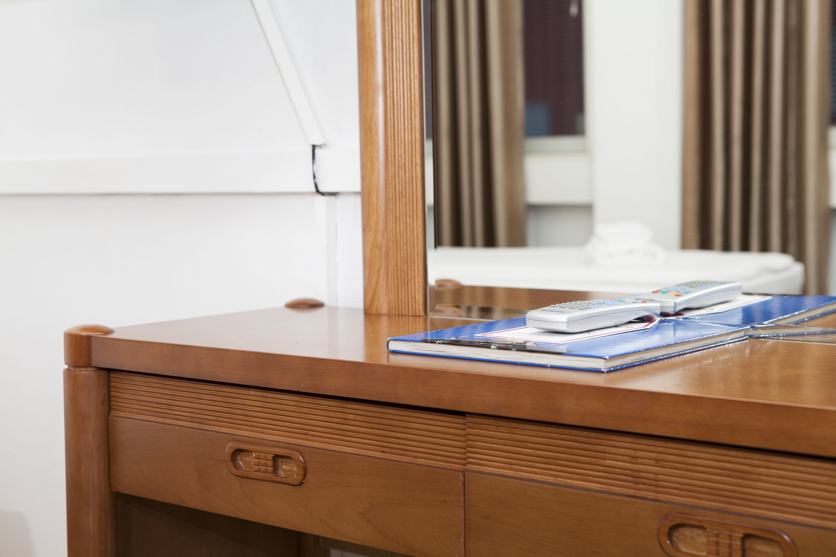 A wooden desk with a mirror, a telephone, and a notebook.
