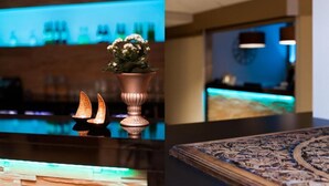 Un espace bar avec un comptoir illuminé de lumière bleue, un vase décoratif rempli de fleurs et une table à motifs au premier plan.