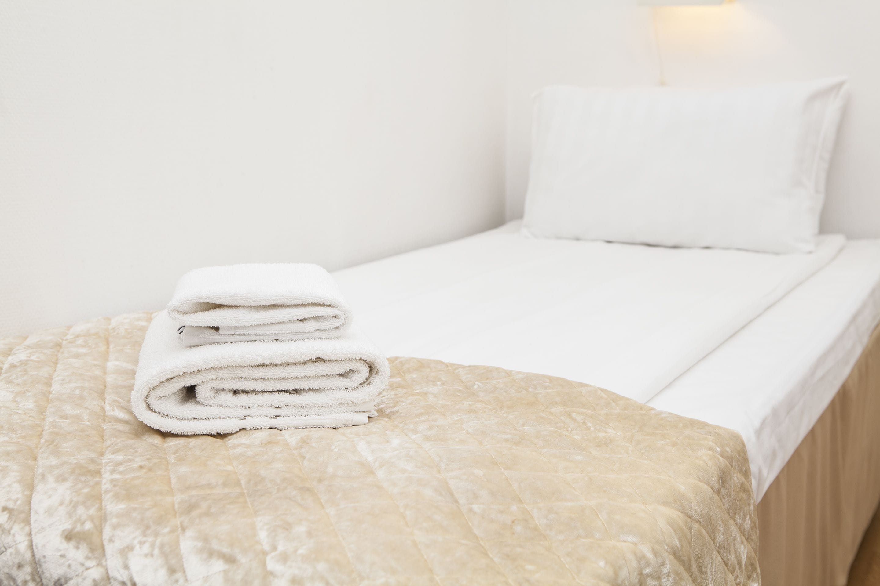 A neatly made bed with a folded white towel on a textured beige bedspread.