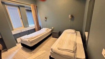 Una habitación de hotel pequeña y con una cama individual, una ventana con persianas, una mesita de noche y una lámpara fijada a la pared.