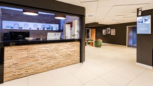 Un espace d’accueil doté d’un comptoir à l’aspect pierre, d’une horloge et d’un panneau indiquant l’emplacement du parking.