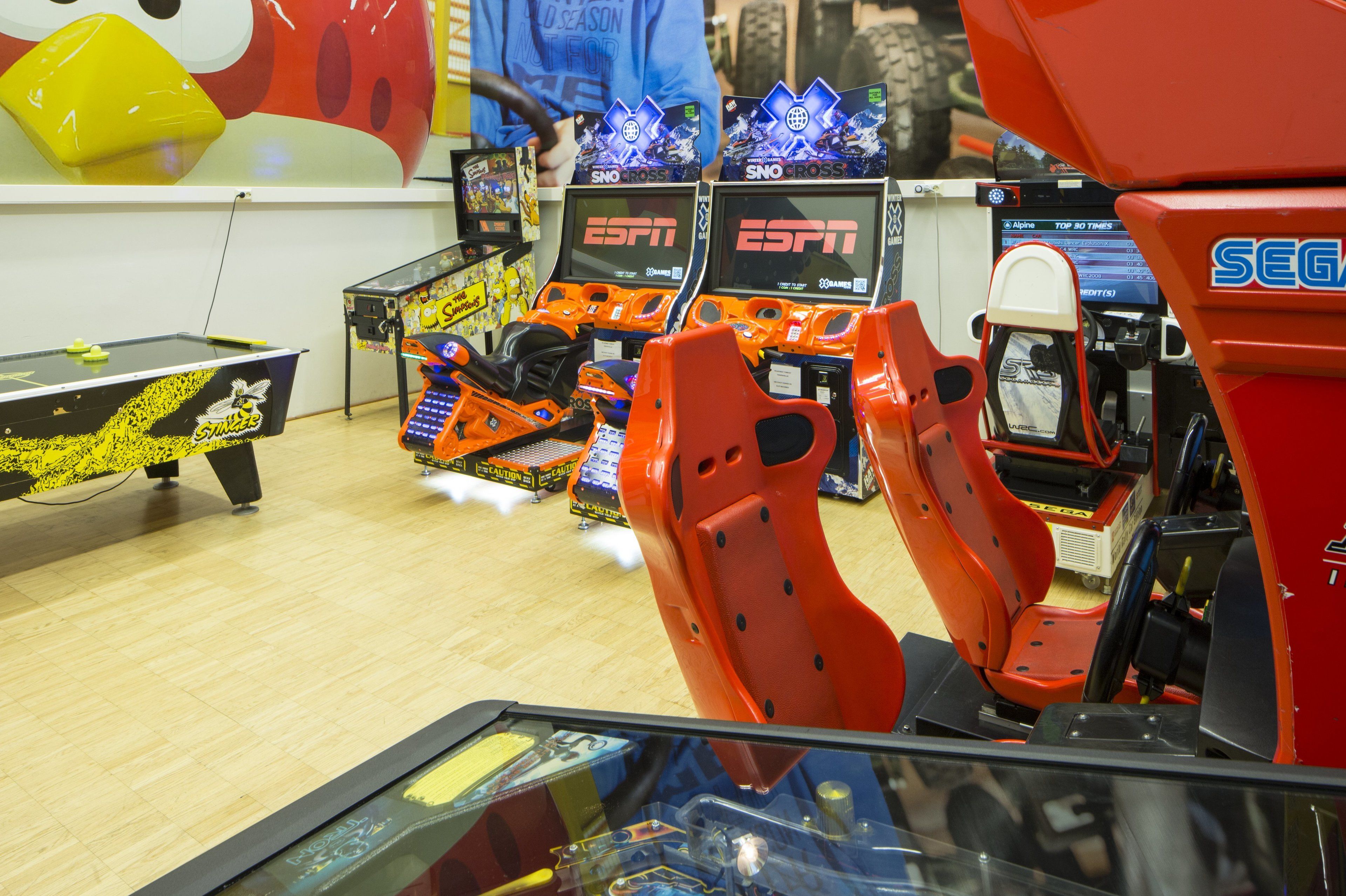 Ein Billardtisch mit gelb-schwarzem Tuch, umgeben von Spielautomaten und einer großen aufblasbaren Figur.