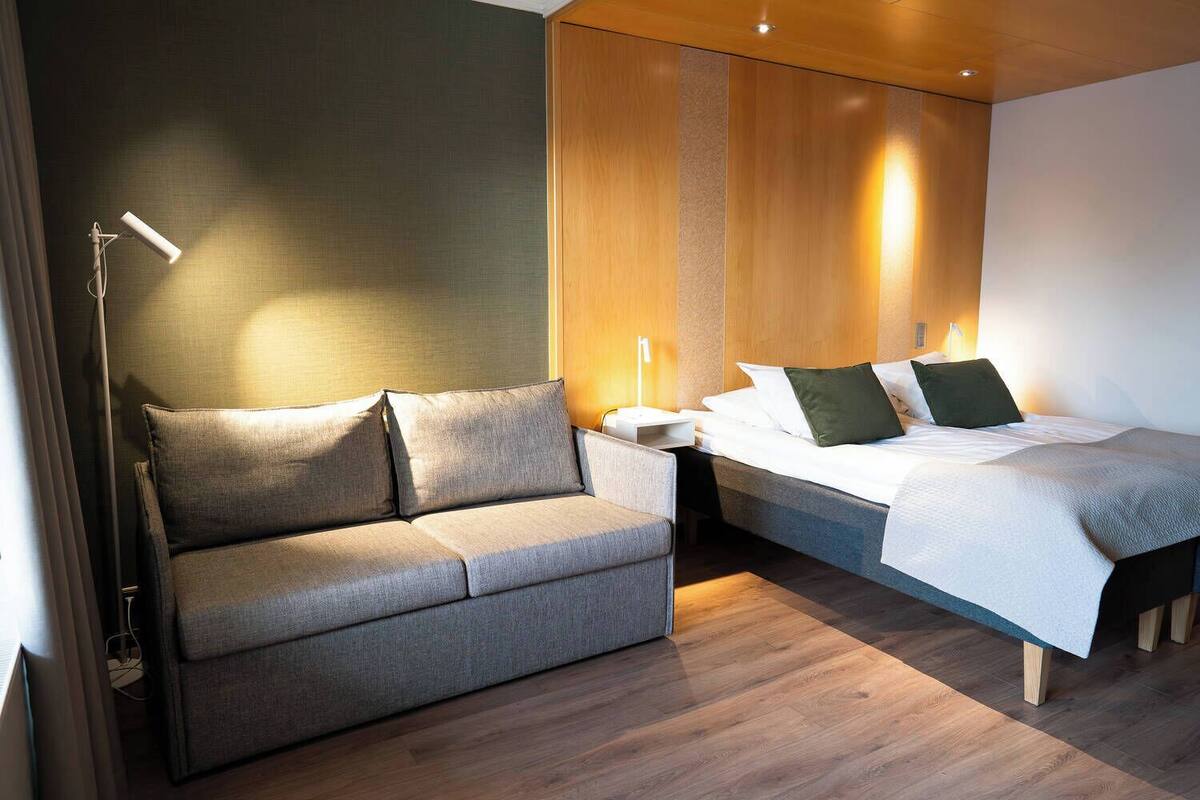 A modern hotel room with a sofa, a bed, and a nightstand.