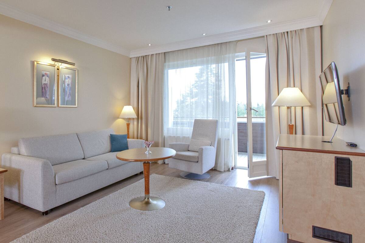 A modern hotel room with a sofa, a round table, a chair, and a bed.