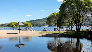 Una playa junto al lago con un pabellón, árboles y gente relajándose junto al agua.
