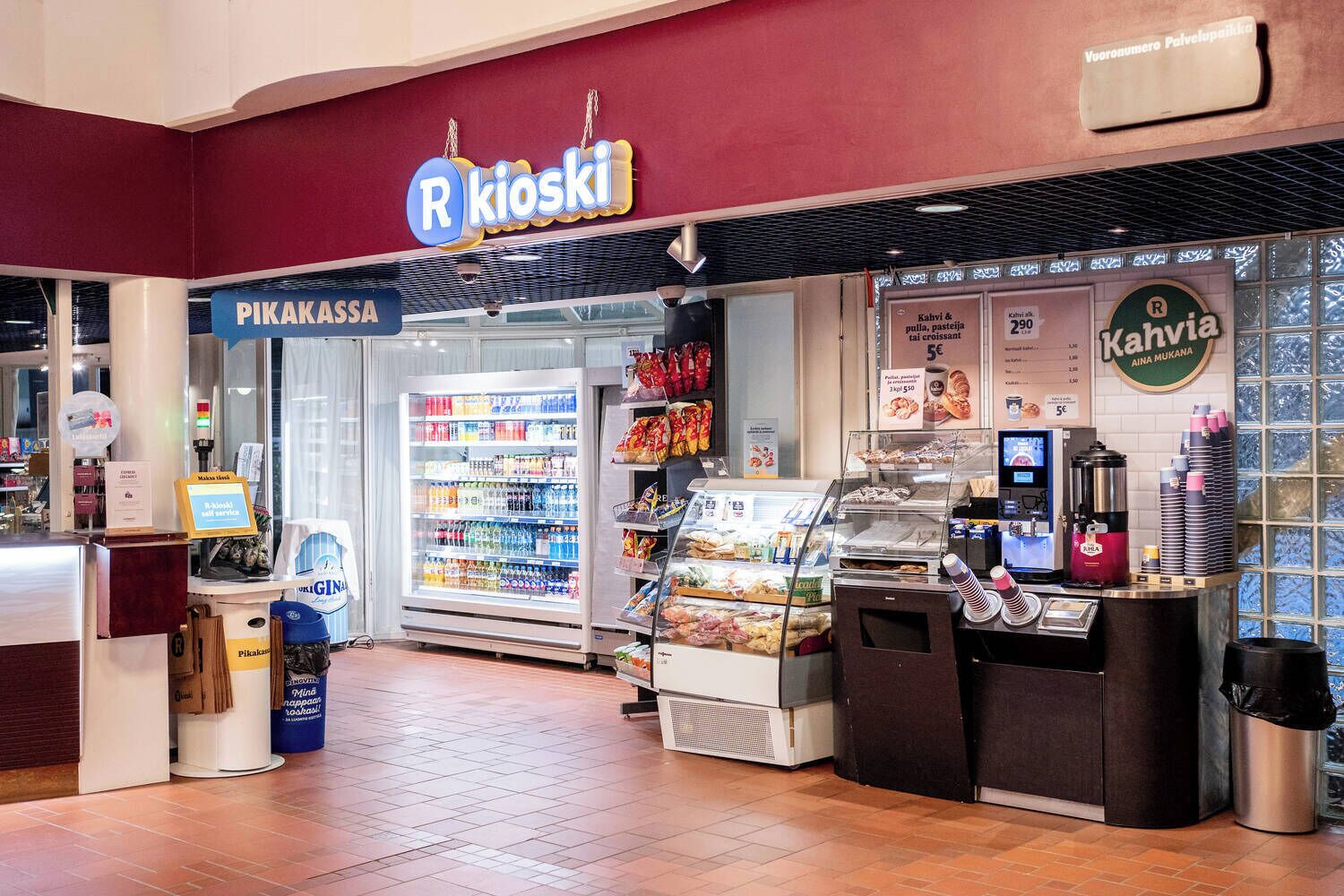 A R Kioski store with a refrigerated display, a coffee machine, and a variety of packaged goods.